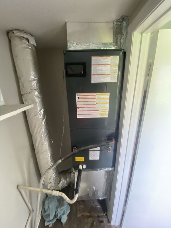 Dark gray air handler installed in a closet with insulated flex duct and PVC condensate drain line