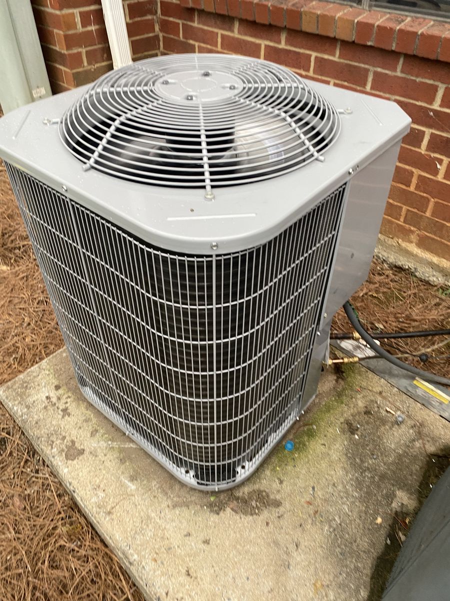 Gray outdoor AC condenser on a concrete pad next to a brick wall