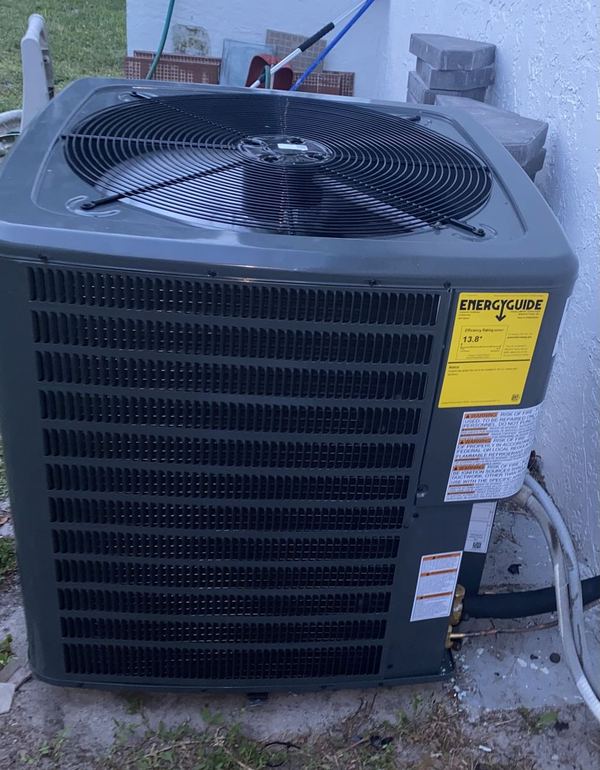 New dark gray AC condenser with its Energy Guide label still attached, installed beside a home