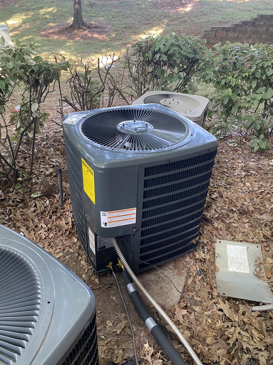 Dark gray outdoor AC condenser on a concrete pad in a mulched side yard, with a second unit nearby