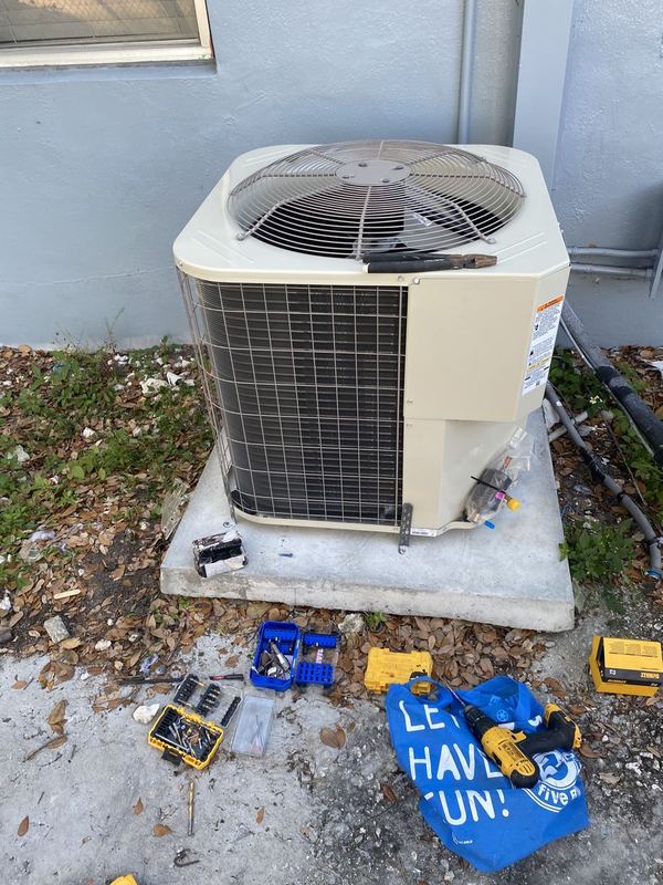 Outdoor AC condenser with tools laid out on the ground during a repair