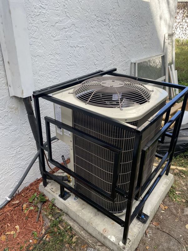 Outdoor AC condenser protected by a black metal security cage on a concrete pad