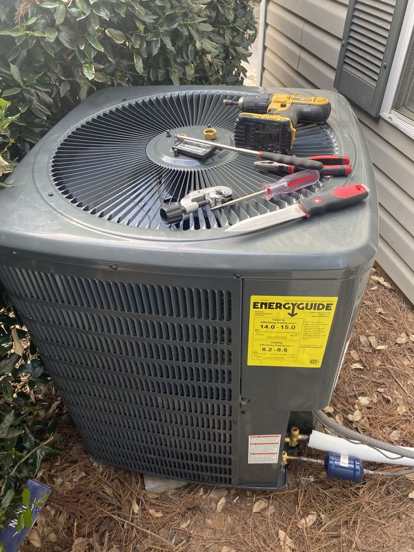 New gray AC condenser with Energy Guide label, tools resting on top during installation