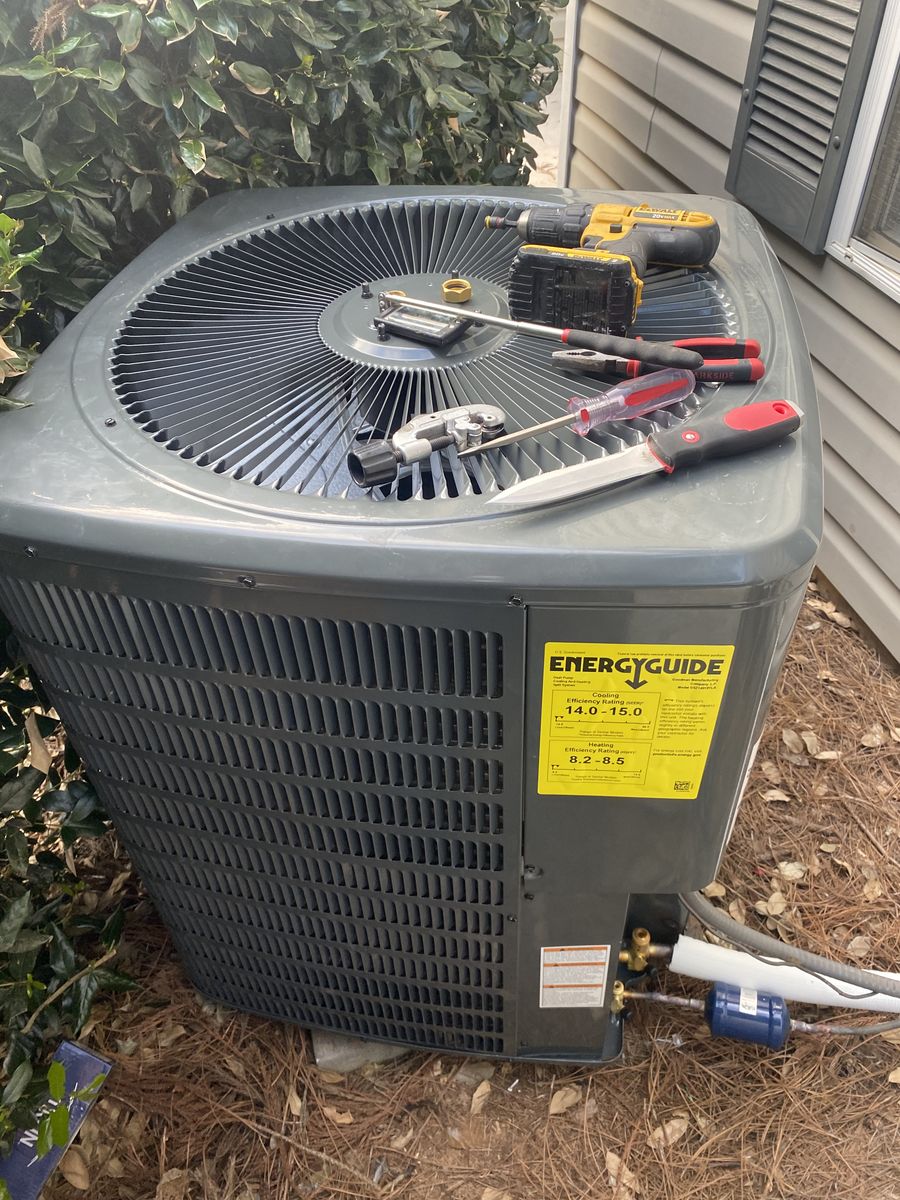 New gray AC condenser with Energy Guide label, tools resting on top during installation
