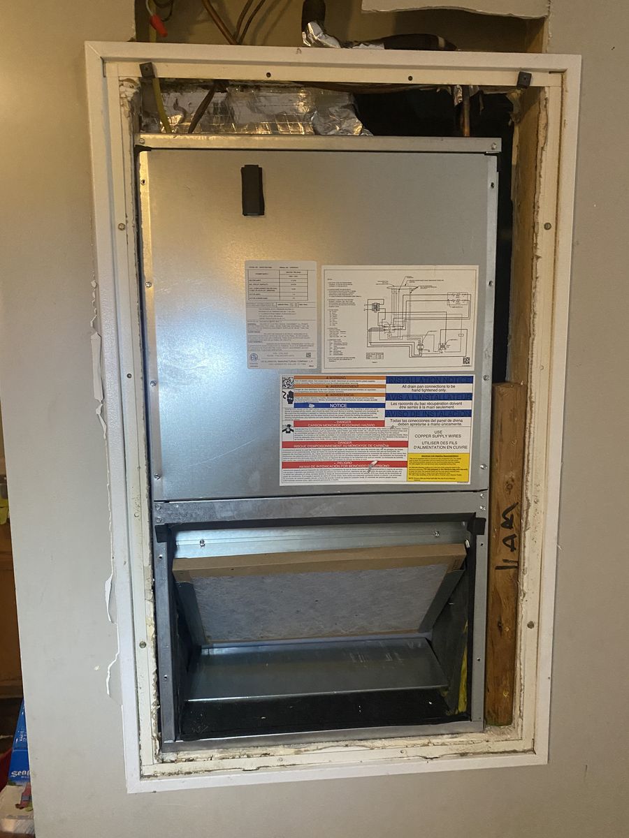 Wall-recessed air handler with the access panel open, showing the unit and the return-air filter rack below